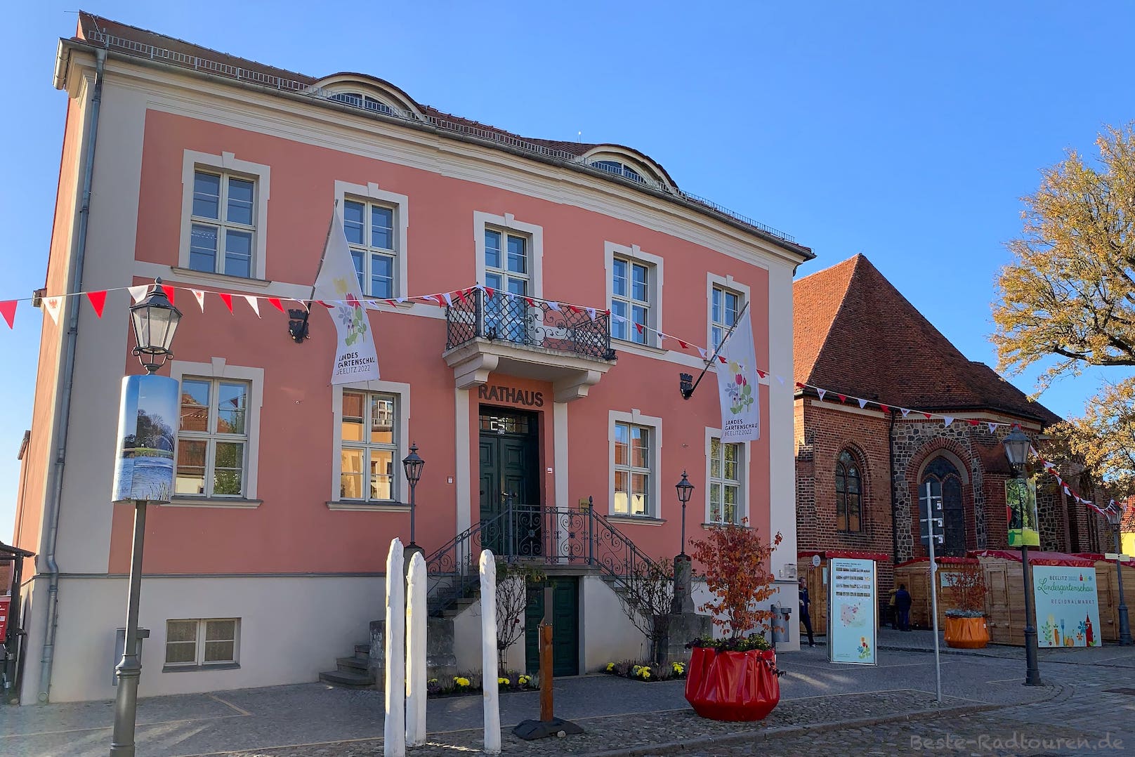 Rathaus von Beelitz mit Fahnen für die Bundesgartenschau 2022; daneben der hintere Teil der Stadtkirche