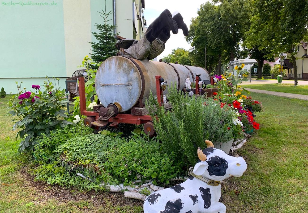Radensdorf (Spreewald): Kunst-Installation mit Güllefass, Schaufensterpuppen, Blumenrabatten, Kuh