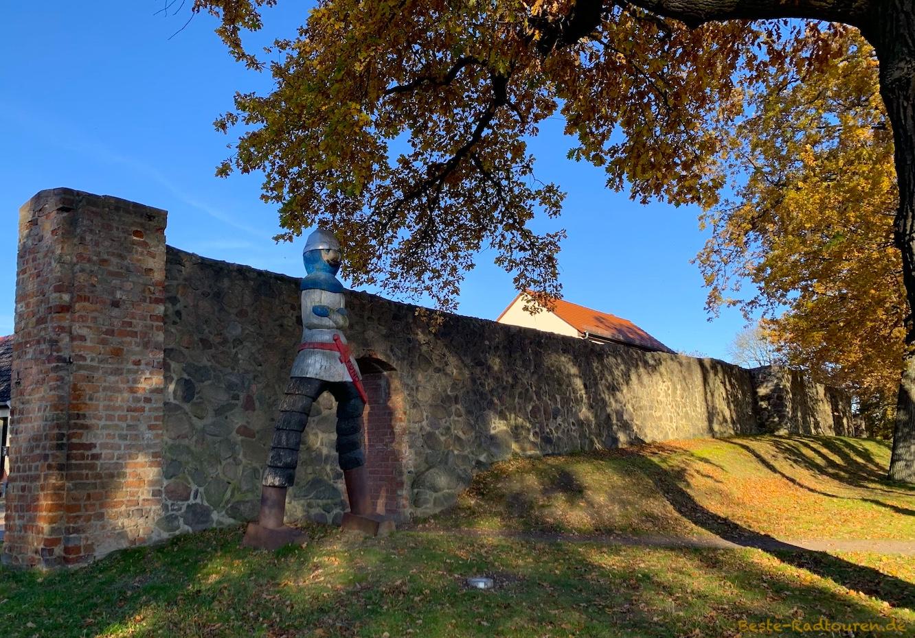Foto vom Radweg aus: Große Ritterfigur aus Holz (Ritter Kuno) steht an der Stadtmauer von Gransee
