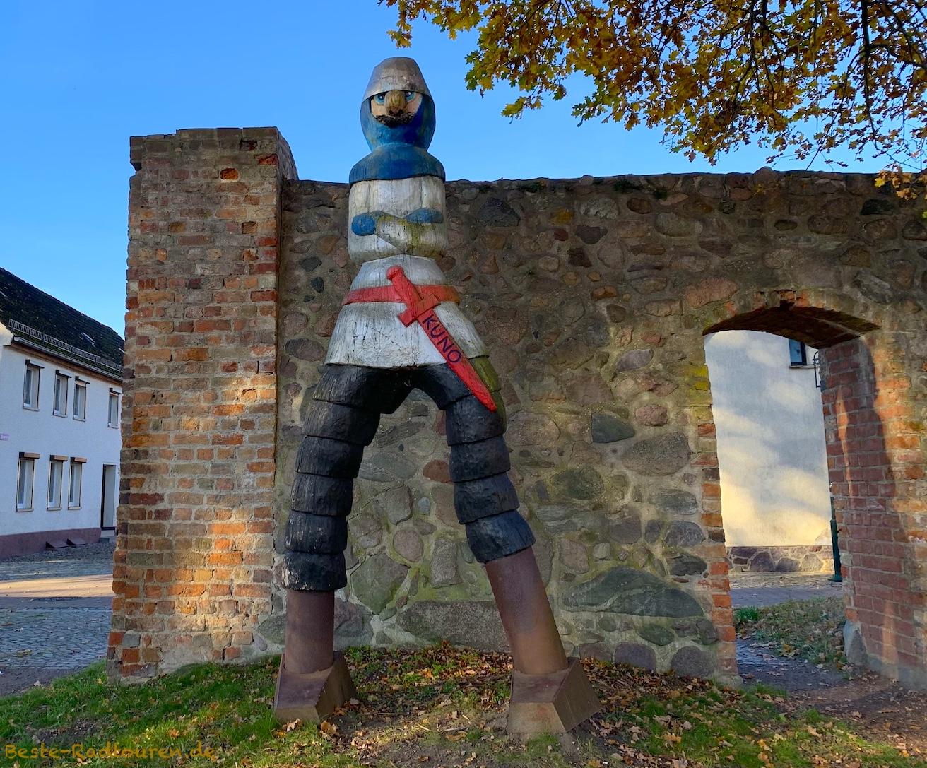 Foto vom Radweg aus: Große Ritterfigur aus Holz (Ritter Kuno) steht an der Stadtmauer von Gransee